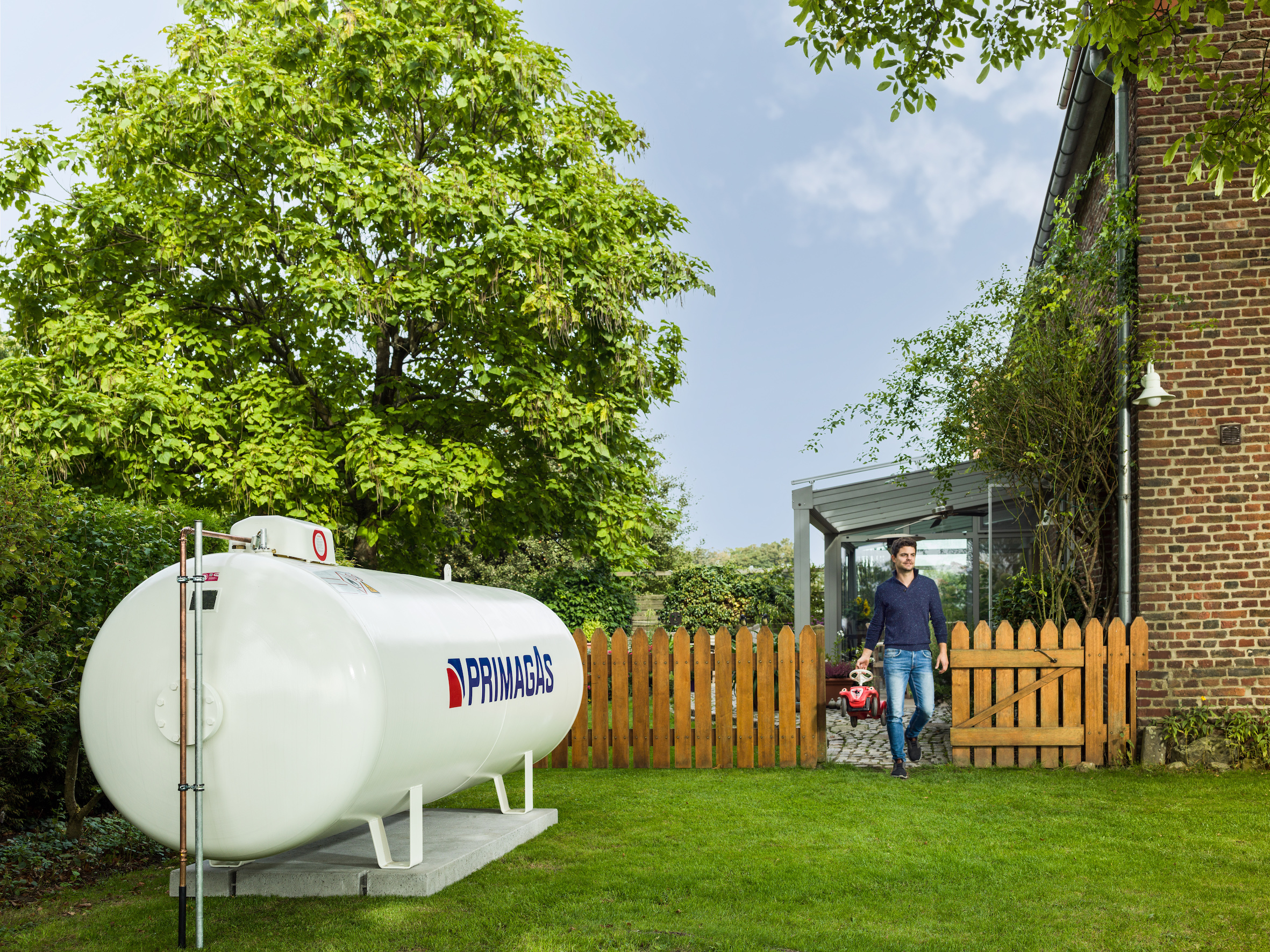 PRIMAGAS - oberirdischer Tank, Garten, Zaun, Mann, Bobycar, Hausecke, Baum, Terrassenüberdachung, 